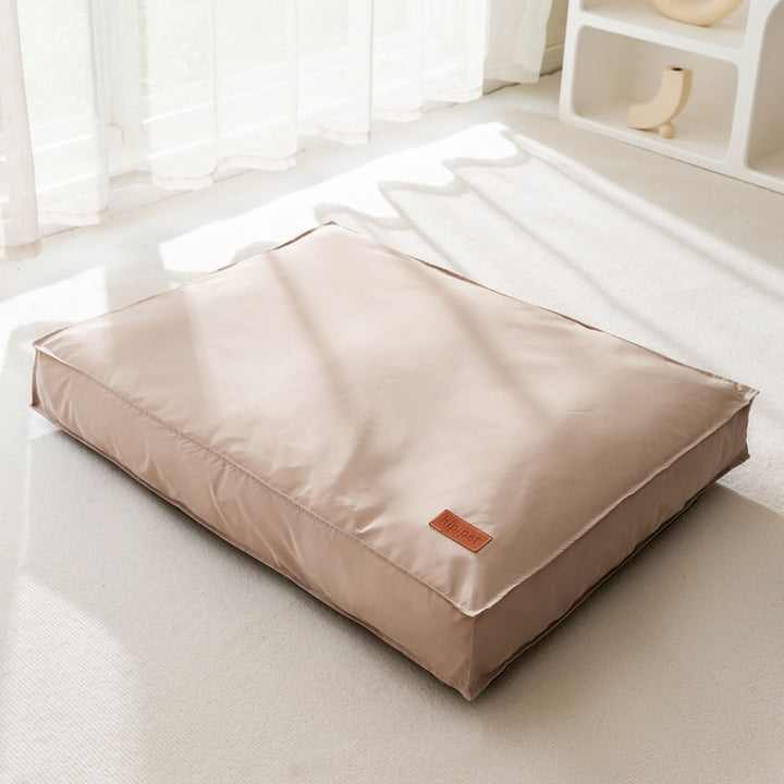 Beige pet bed with a small brown label on a light wooden floor.